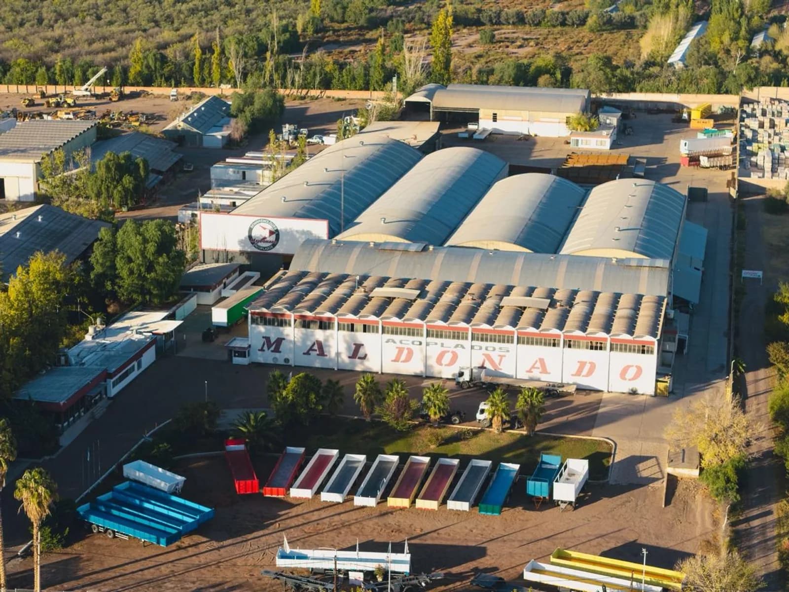Vista aérea de la planta Maldonado en Mendoza: naves de producción, la fila de bateas de colores terminadas y la montaña al atardecer.