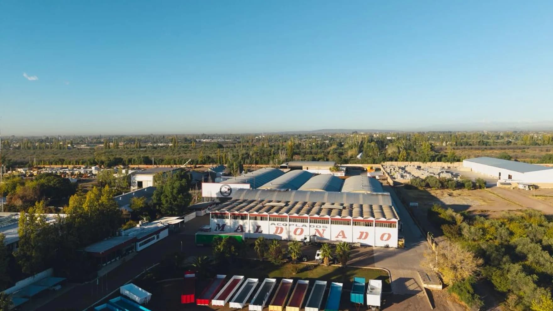 Vista aérea panorámica de la planta Maldonado en Mendoza: naves de producción, el cartel MALDONADO ACOPLADOS y la fila de unidades terminadas.